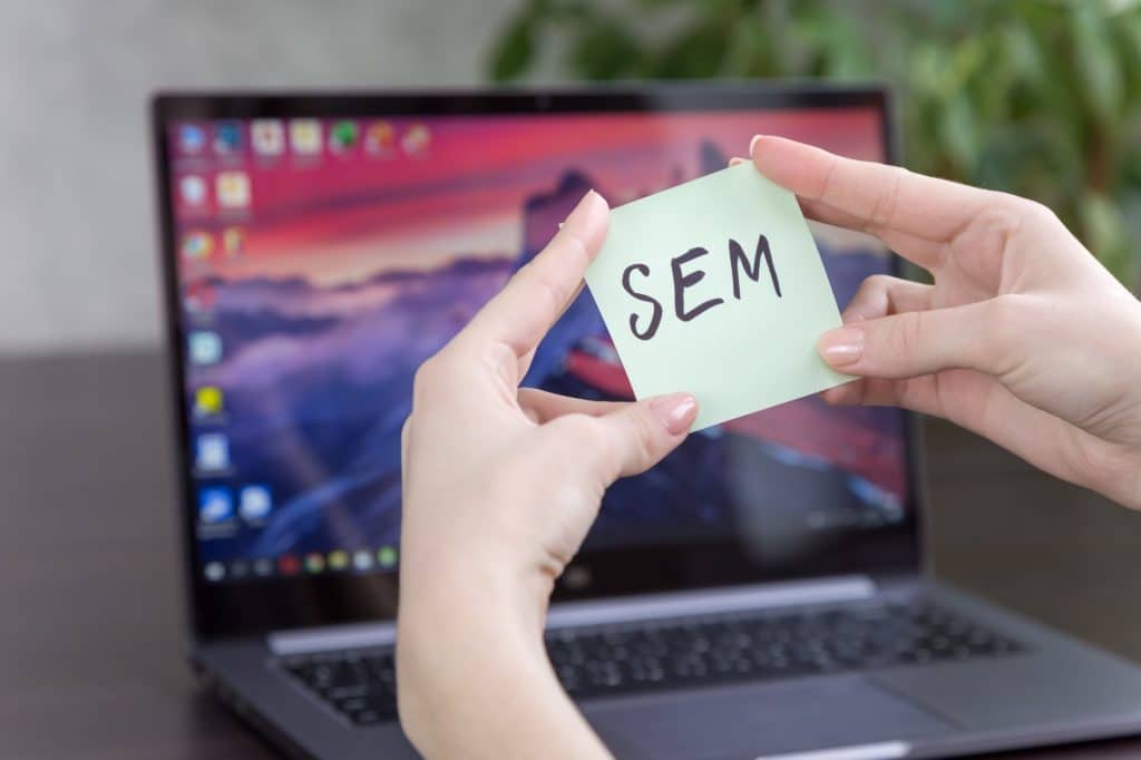SEM inscription on a note sheet in female hands on the background of a laptop , soft focus