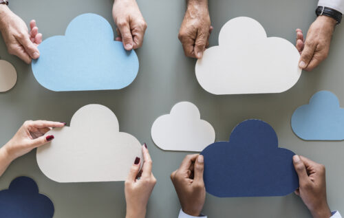 Hands hold various-colored clouds in front of a gray background to debate between AWS vs Azure