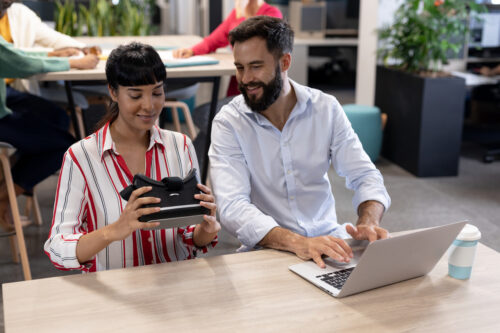 Two people sit at a table with a computer and VR headset